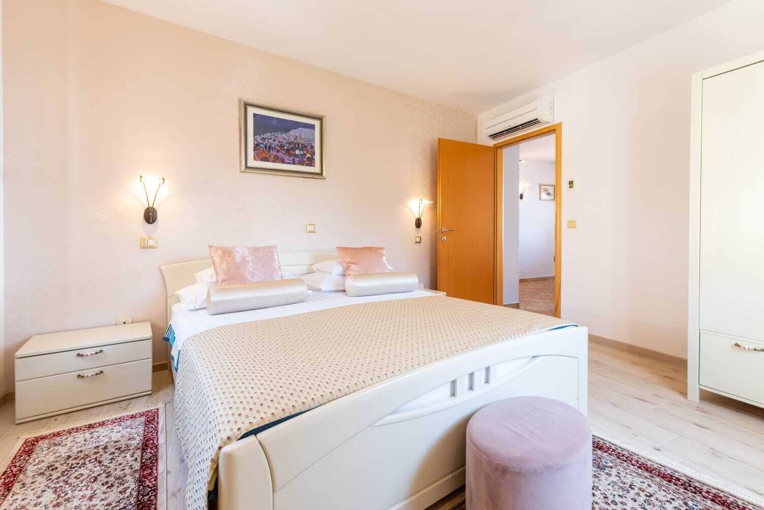 Ein Schlafzimmer mit Bett, Nachttischen, einem Kleiderschrank, einer Tür und einem Wandbild.