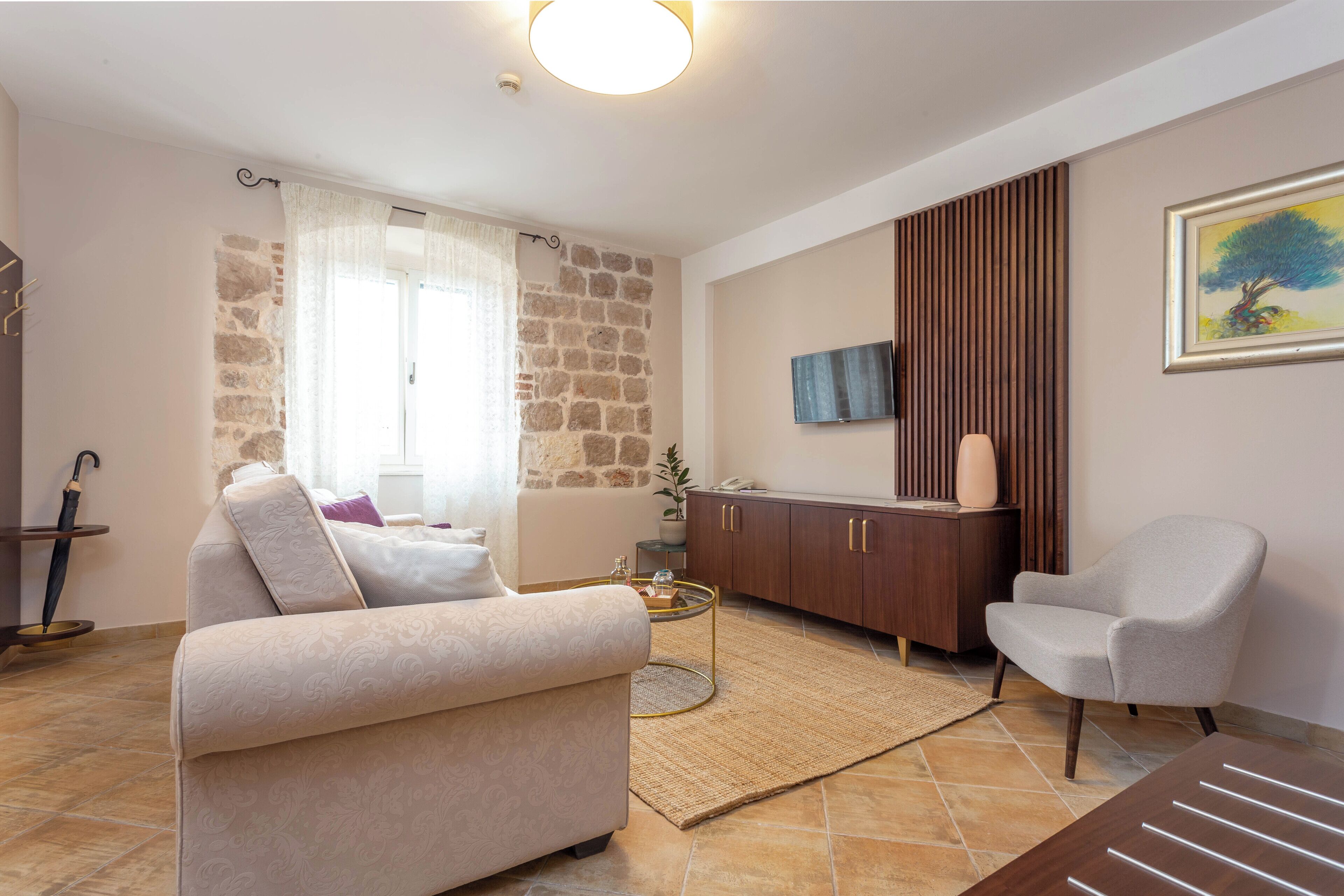 A living room with a sofa, armchair, coffee table, and a TV mounted on the wall.