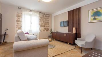 A living room with a sofa, armchair, coffee table, and a TV mounted on the wall.