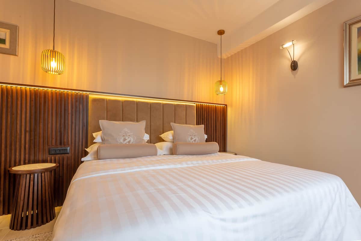 A neatly made bed with a striped bedspread, a wooden headboard with vertical slats, and two wall-mounted light fixtures.