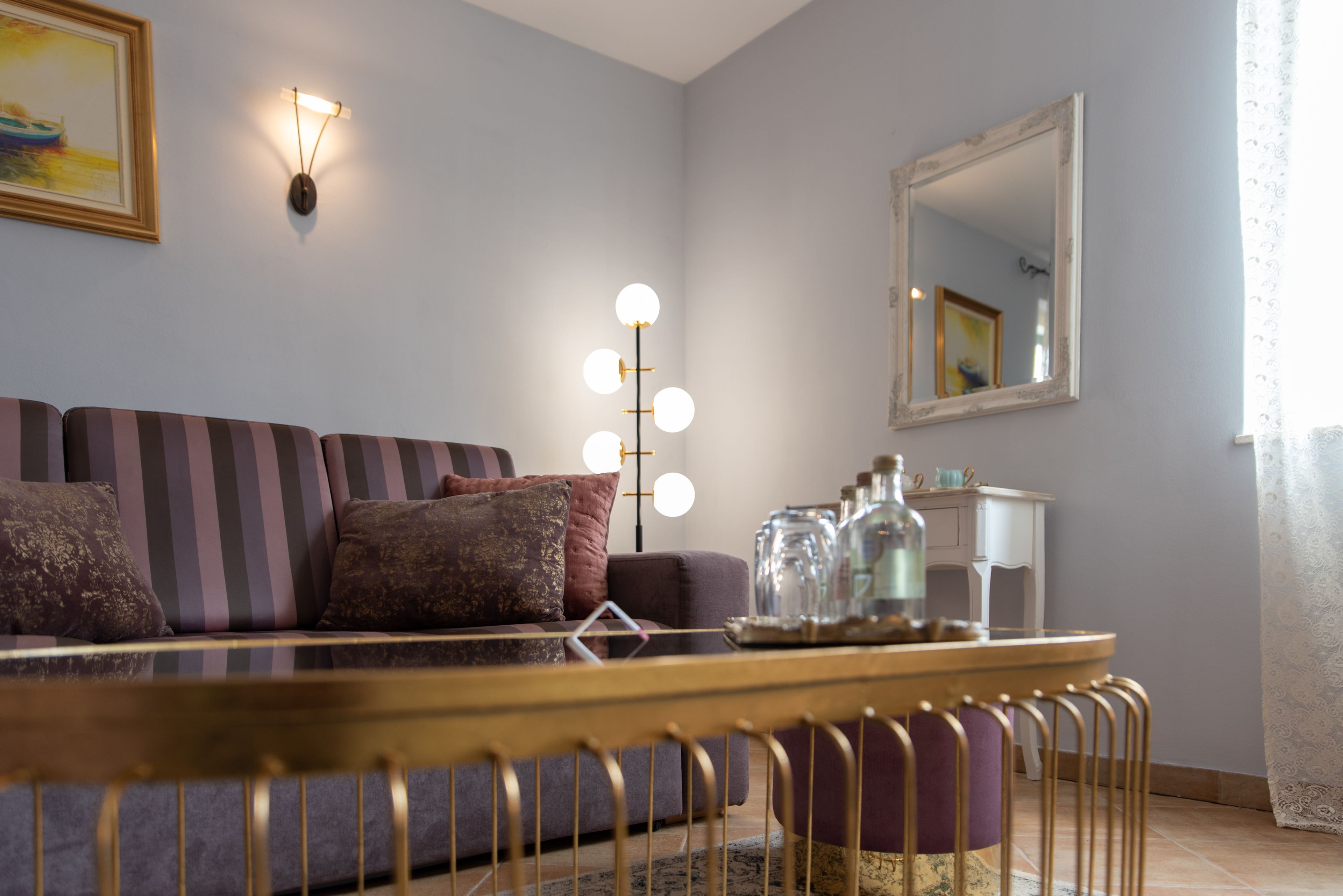 Ein Wohnzimmer mit einer Couch, einem Couchtisch, einer Lampe, einem Spiegel und einem Fenster mit Vorhängen.