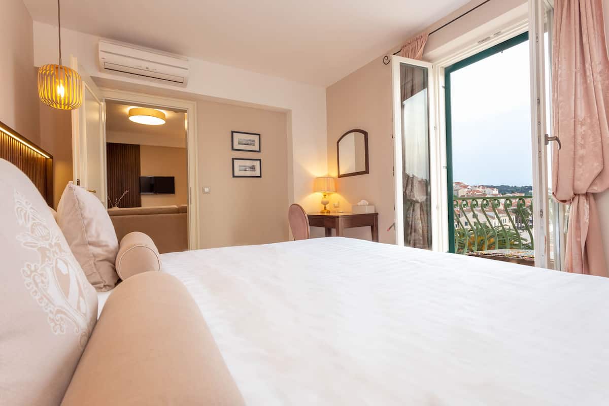 A hotel room with a bed, a desk, a chair, a lamp, a mirror, and a view of the outside.