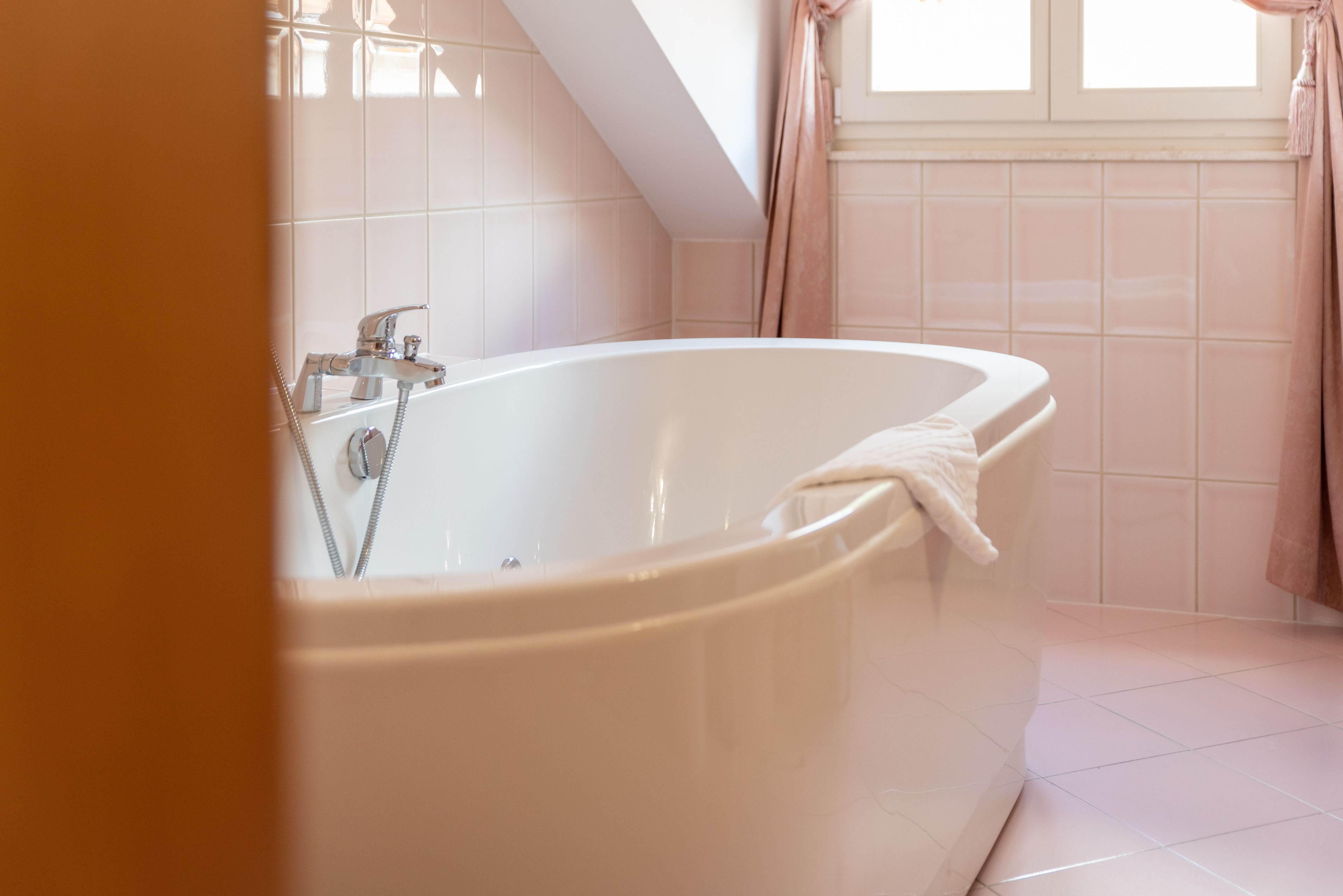 Un baño moderno con una bañera independiente, una ventana con cortinas y paredes de azulejos blancos.