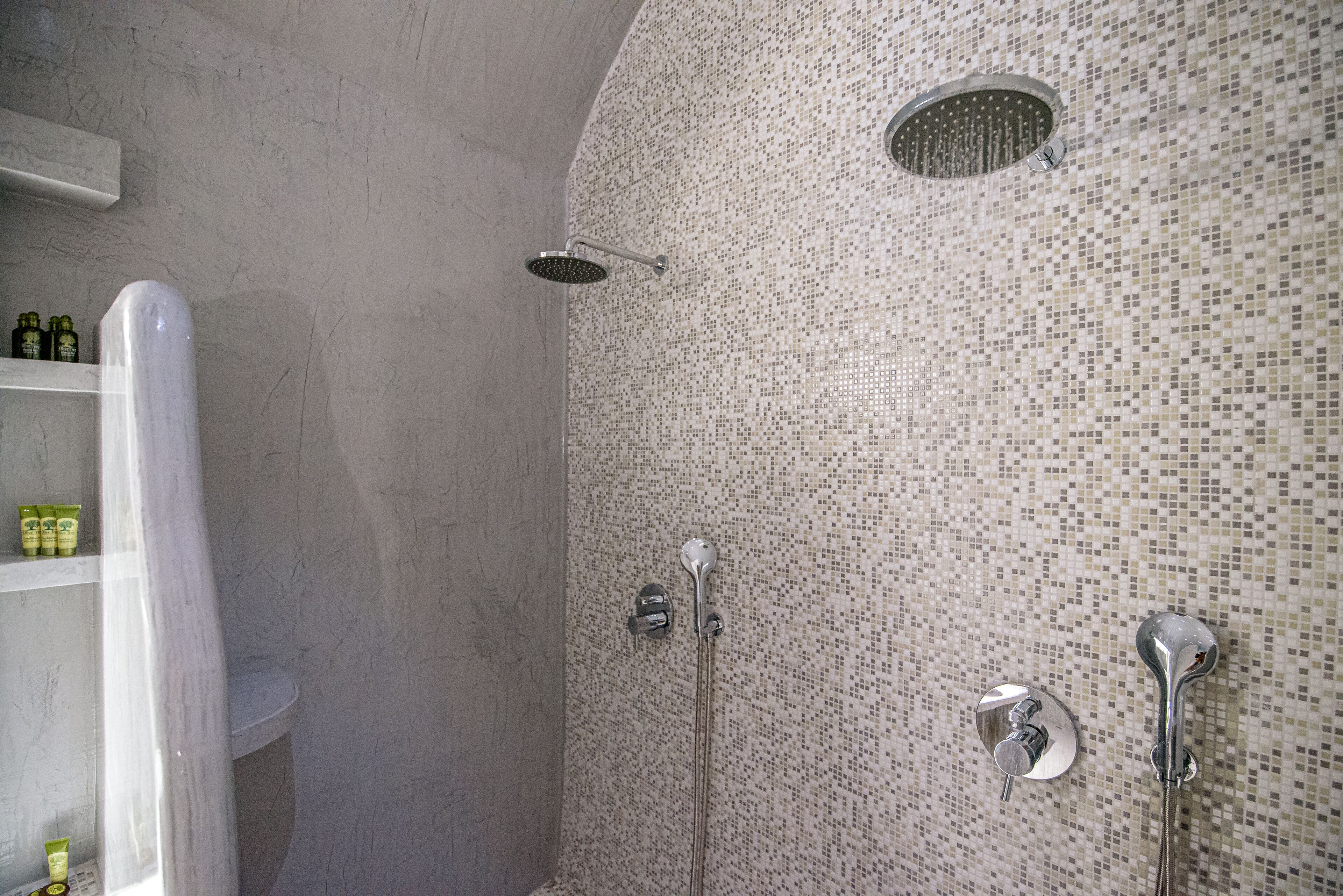 A shower with a mosaic tile wall, a white bathtub, and a shelf with toiletries.