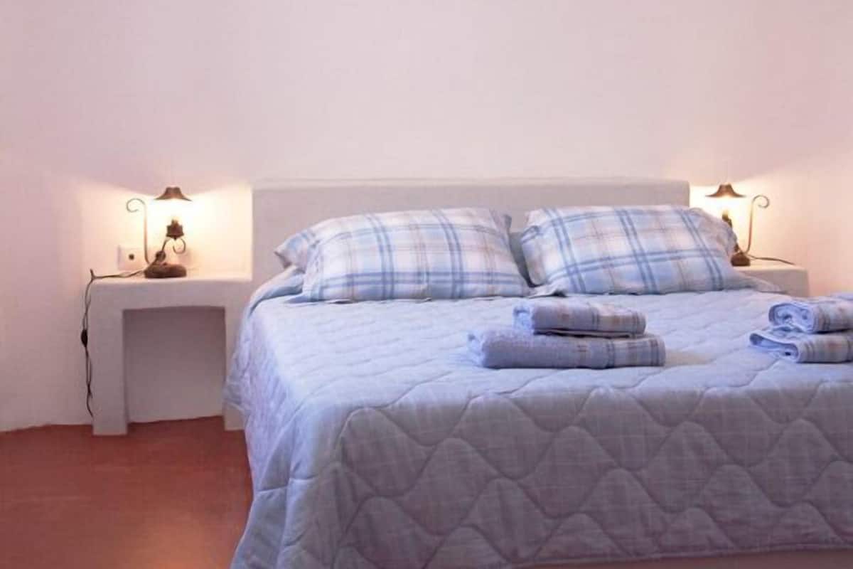 A neatly made bed with a quilted cover and two pillows, flanked by bedside tables with lamps.