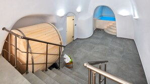 A modern interior with a wooden barrel, a staircase, and a small table with towels and fruit. - Anatoli Hotel and Spa (Santorini)