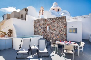 Une terrasse sur le toit, avec un mur en pierre, un jacuzzi et une table dressée pour le dîner.