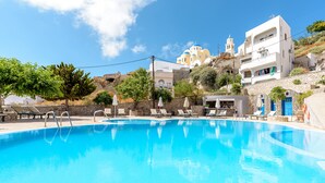 A clear blue swimming pool with lounge chairs and umbrellas, surrounded by stone walls and buildings with white and blue domes. - Anatoli Hotel and Spa (Santorini)