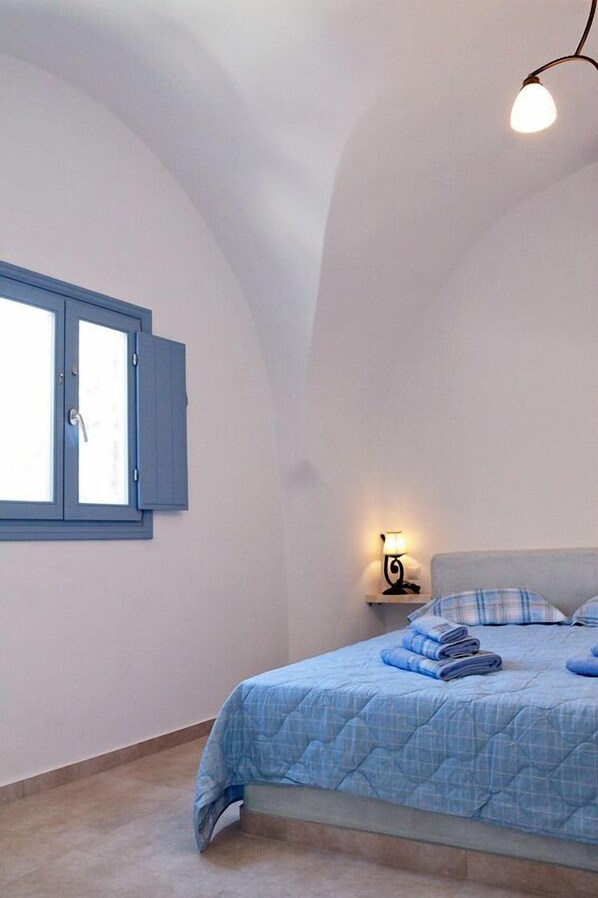 A bedroom with a bed, a window with blue shutters, a wall-mounted lamp, and a ceiling light.