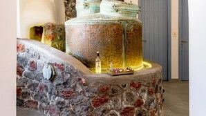 A stone fountain with a tiered design, a stone wall, and a door in the background. - Anatoli Hotel and Spa (Santorini)