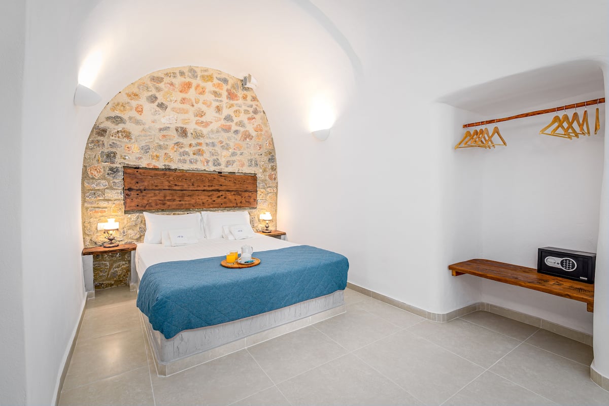 A bedroom with a stone arch, a bed with a blue blanket, a wooden headboard, bedside lamps, and a wooden shelf with a radio.