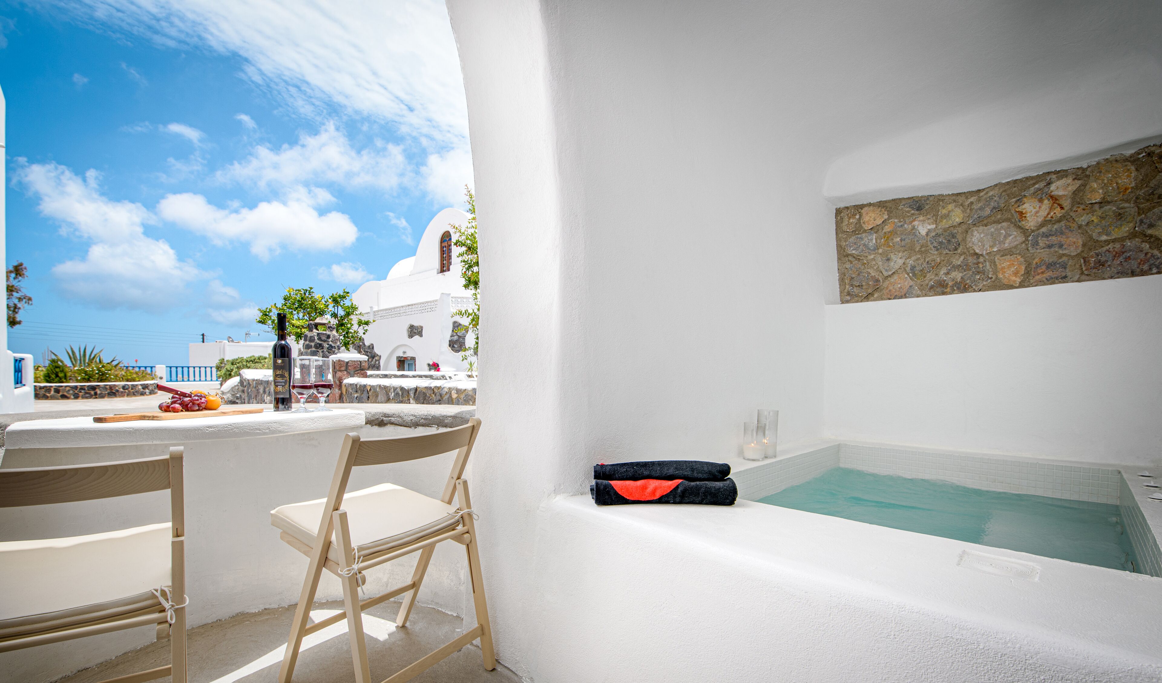 Une pièce aux murs blancs, avec un mur en pierre, une baignoire et une table sur laquelle se trouvent une bouteille et des verres.