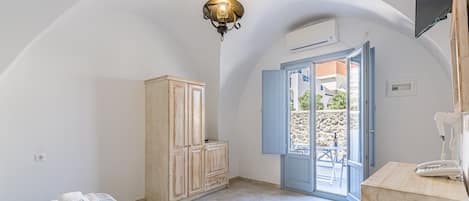 A room with a bed, a wardrobe, a desk with a telephone, and a door leading to an outdoor area.