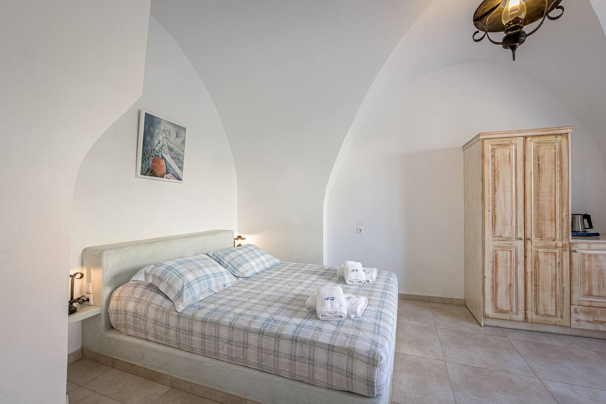 A bedroom with a bed, a nightstand, a lamp, a wardrobe, and a painting on the wall.