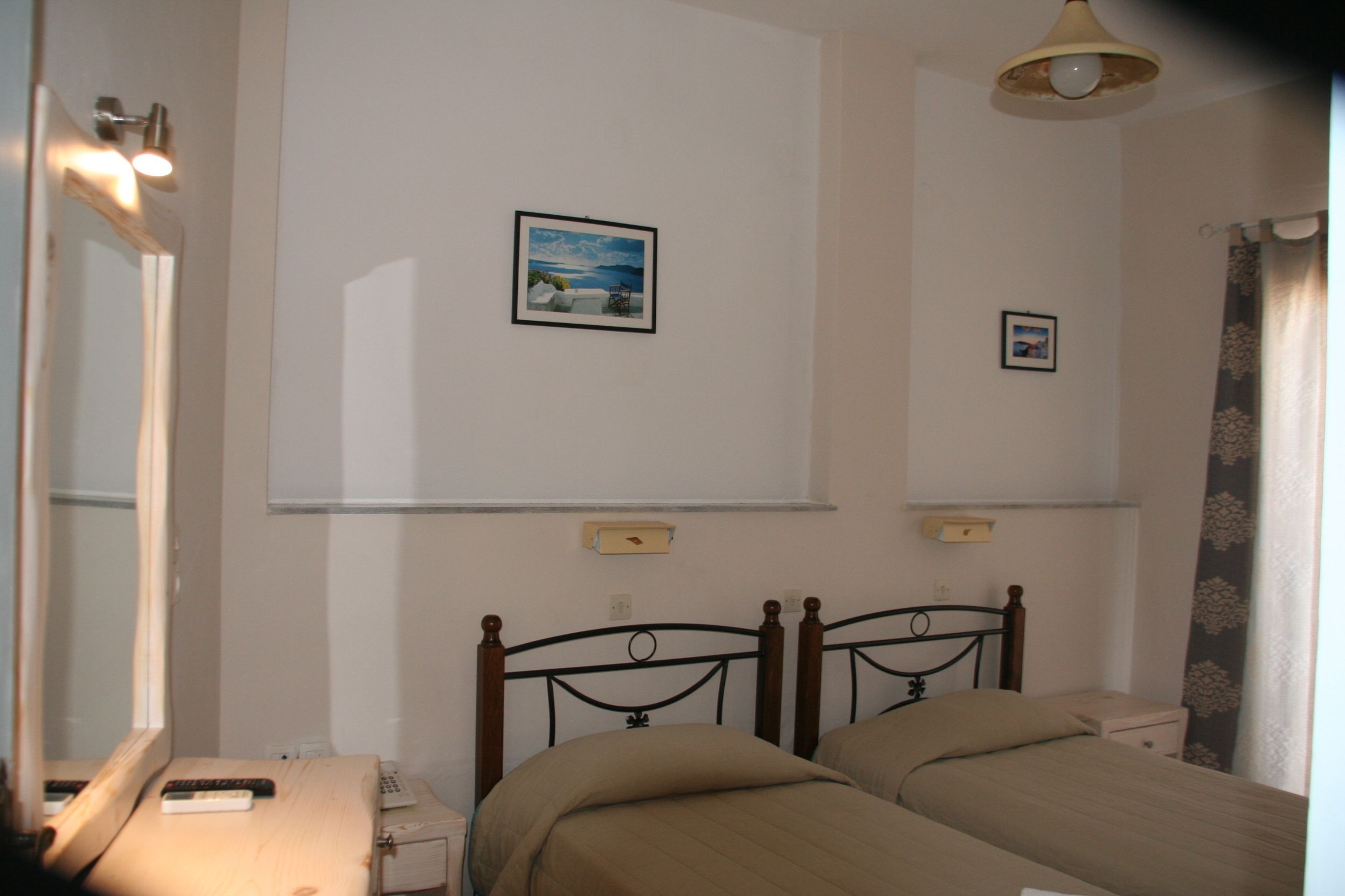 A bedroom with two beds, a bedside table, a mirror, and a ceiling light.