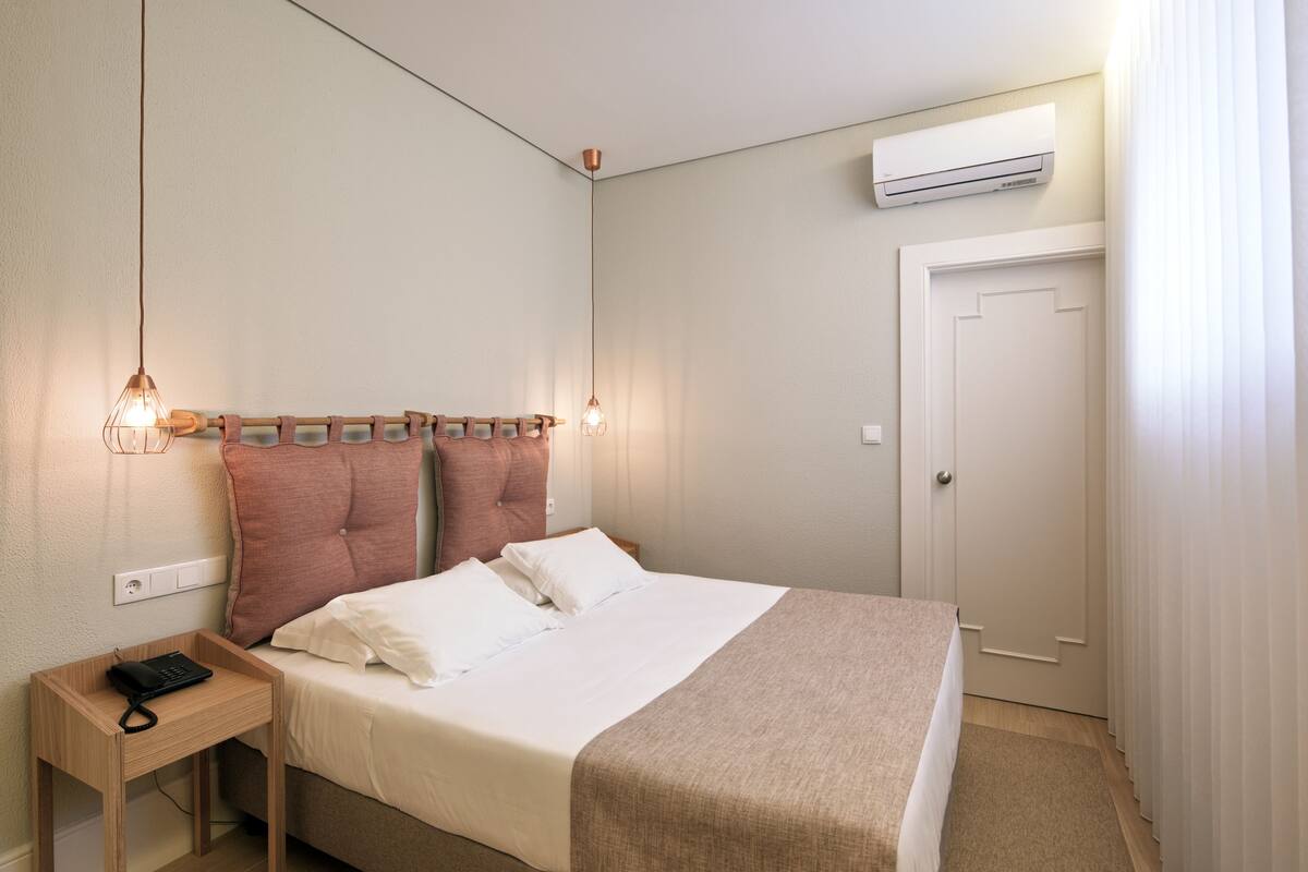 A neatly arranged bedroom with a bed, bedside table, and an air conditioning unit.