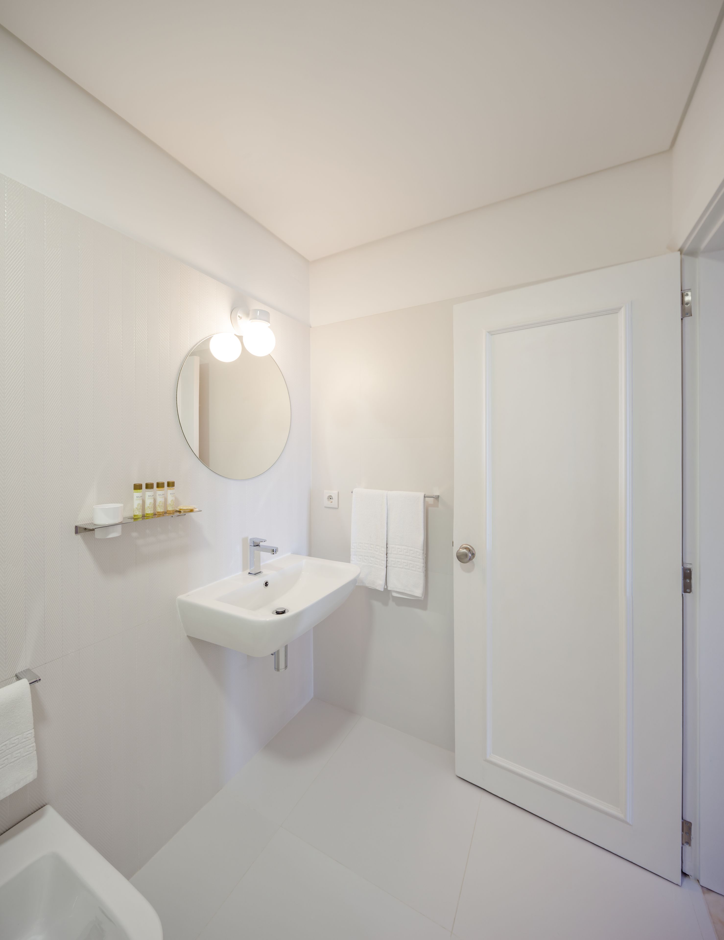 A modern bathroom with a white sink, mirror, and toilet. There is a towel rack with a towel hanging on it.