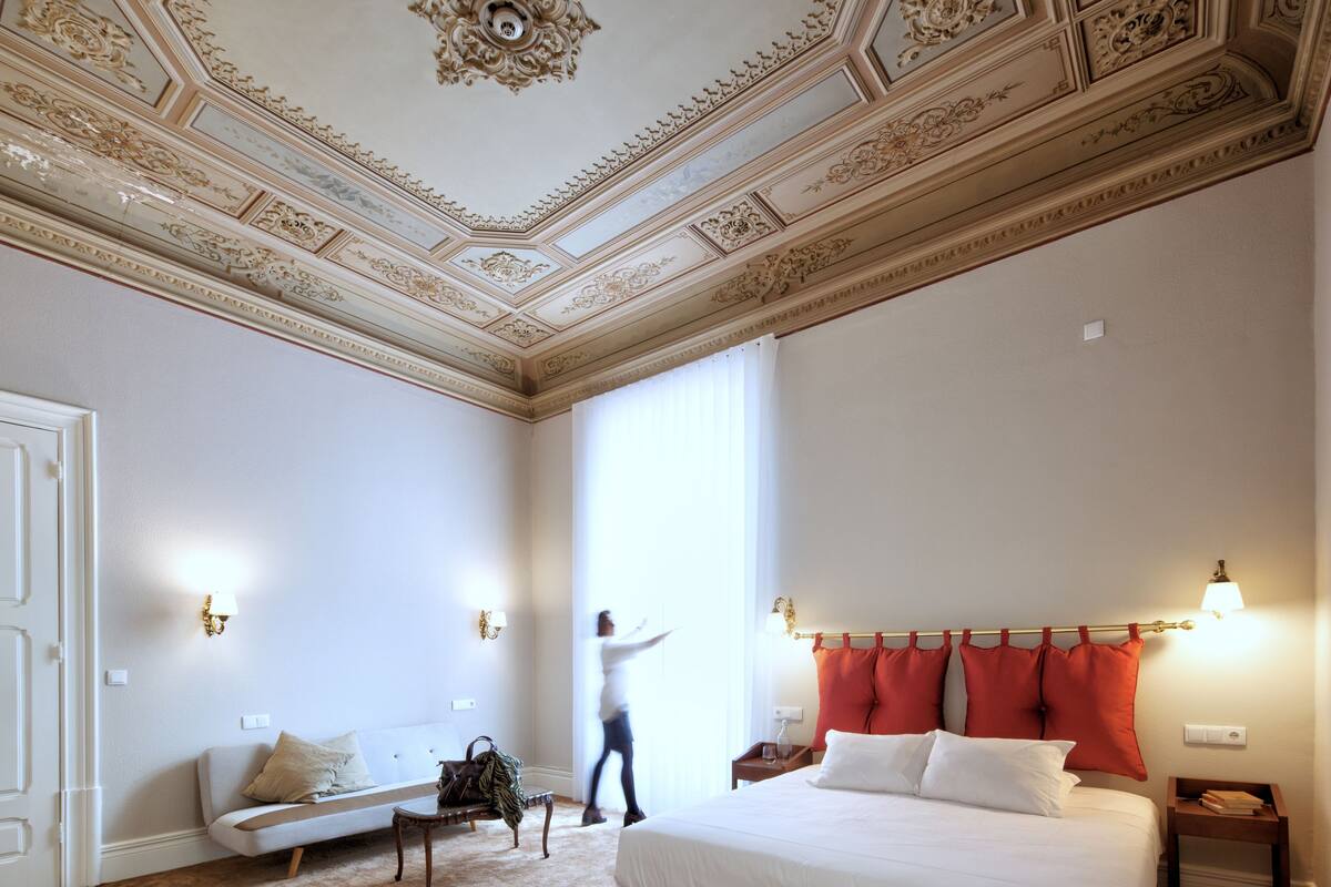 A hotel room with a large bed, a sofa, a small table, and a decorative ceiling.
