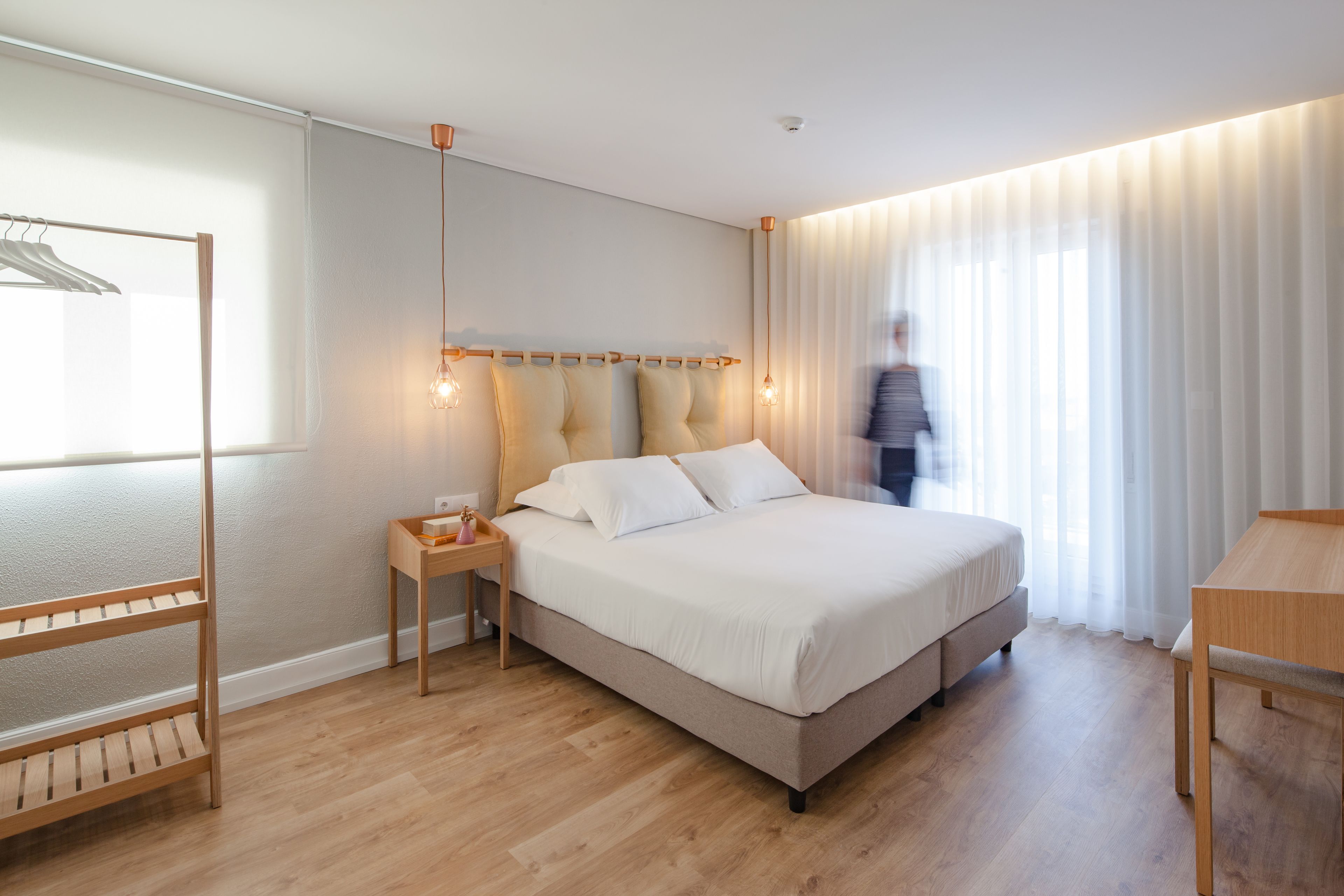 A modern hotel room with a bed, bedside table, and a wooden chair.
