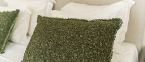 A bed with white linens and a green textured pillow.