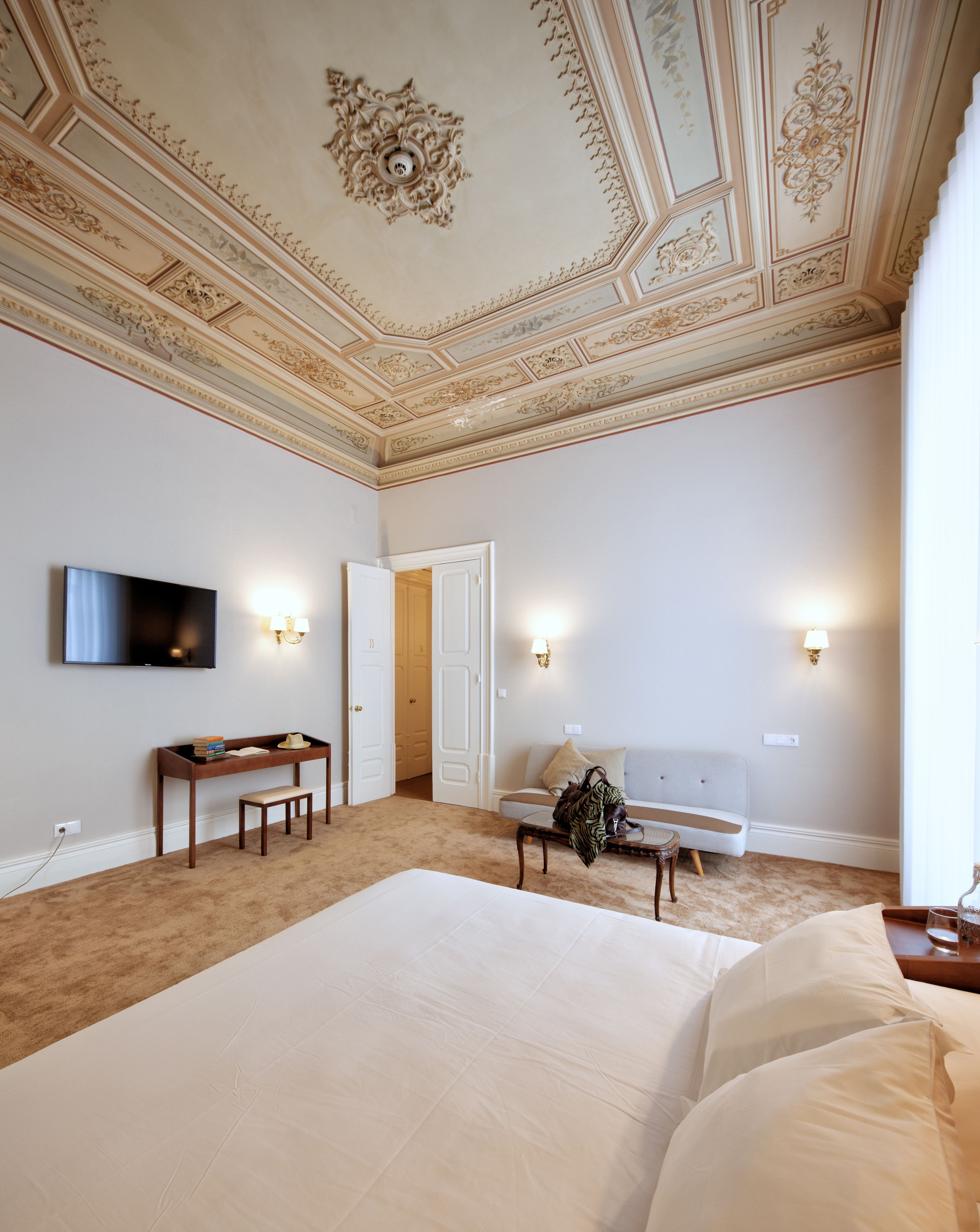 Une chambre d’hôtel avec un grand lit, un bureau avec une chaise, une télévision et deux lampes fixées au mur.