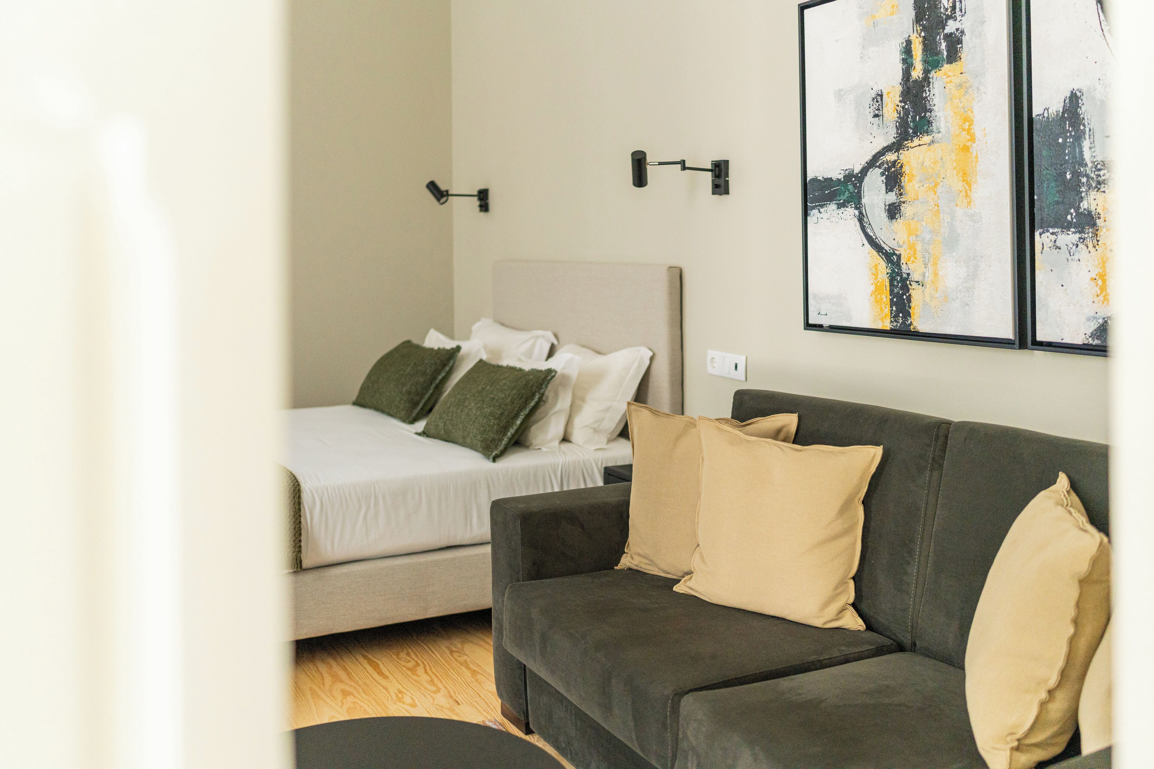 Una camera da letto moderna con un letto, un divano grigio e arte astratta appesa al muro.