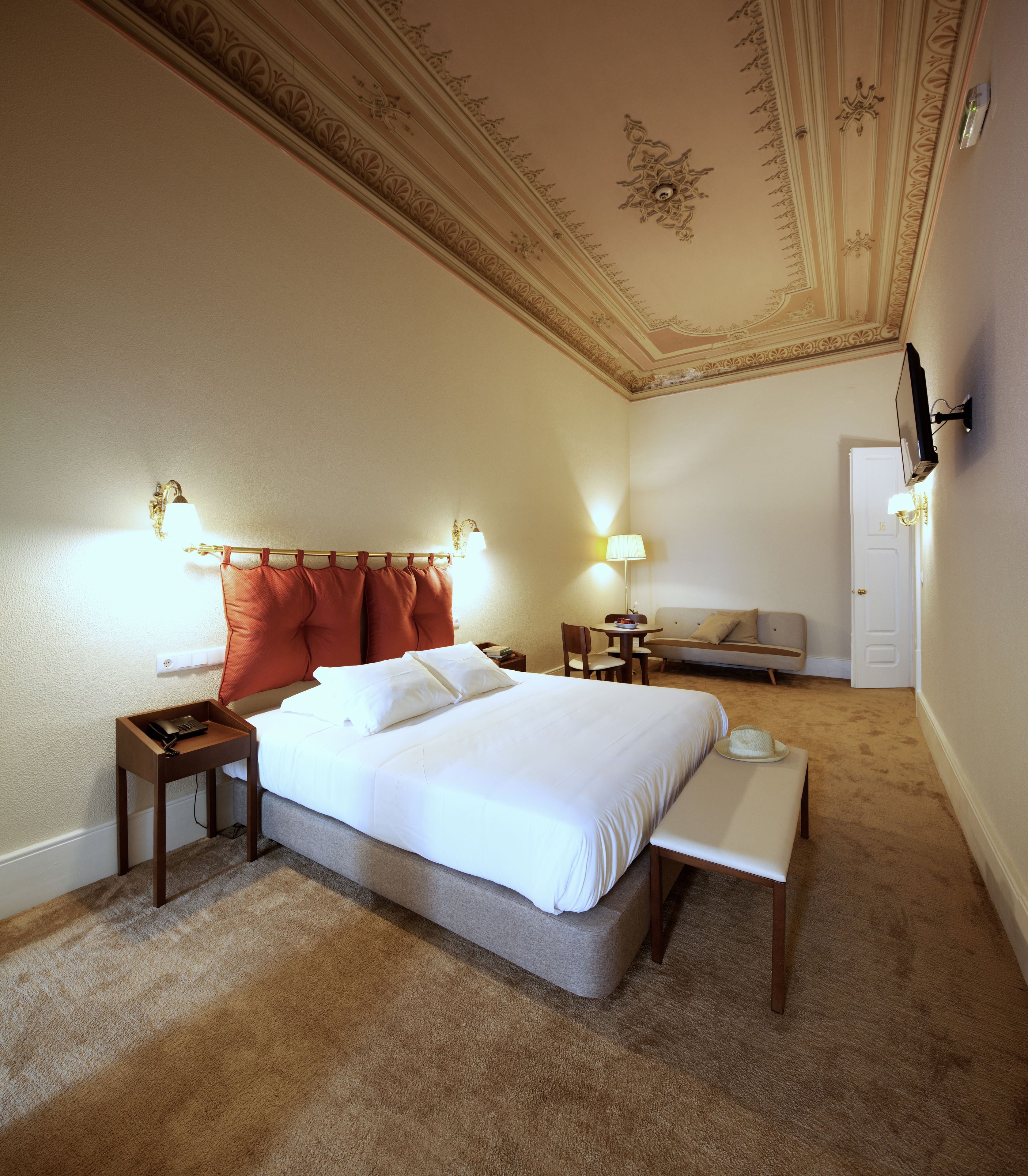 A hotel room with a large bed, bedside tables, a desk, a chair, a lamp, and a television mounted on the wall.