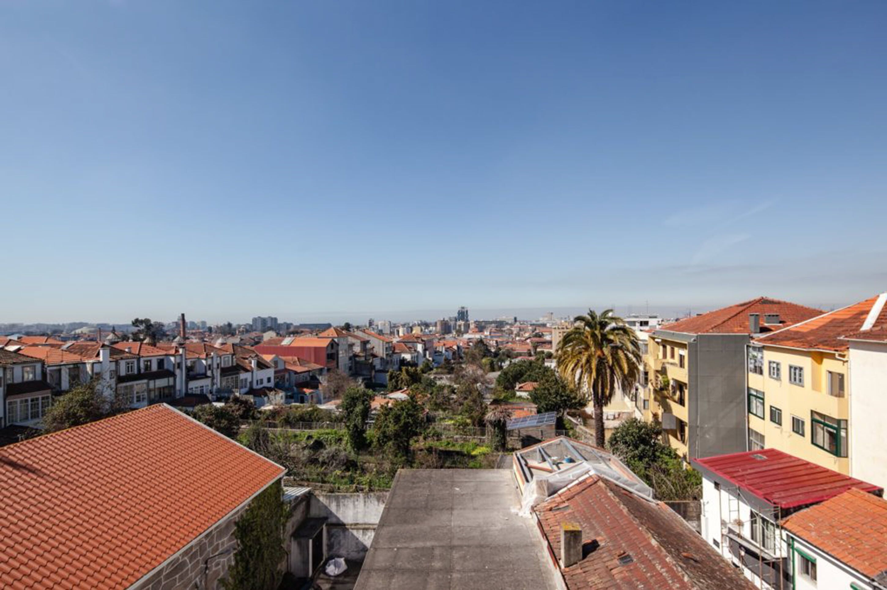 Área residencial com telhados de cerâmica vermelha, diversos estilos de construção e céu claro.