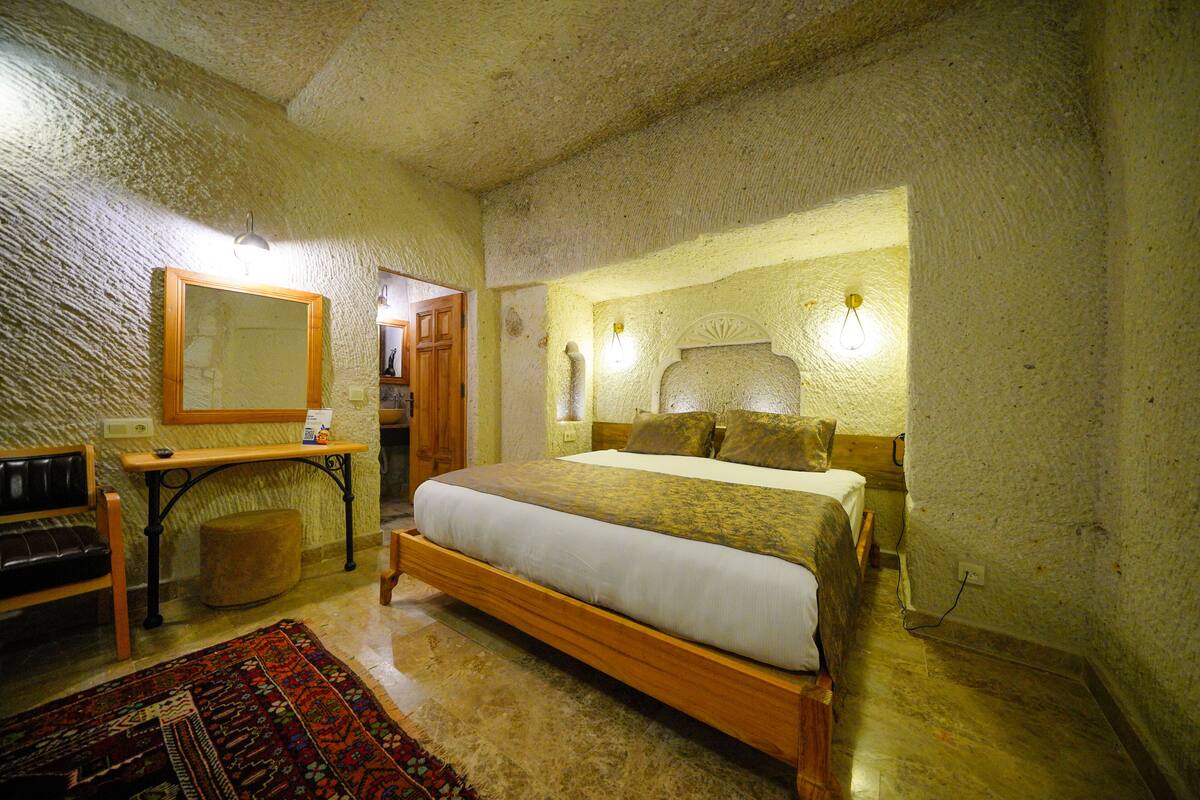 Ein Schlafzimmer mit einem hölzernen Bett, einem kleinen Tisch, einem Spiegel und einem gemusterten Teppich.