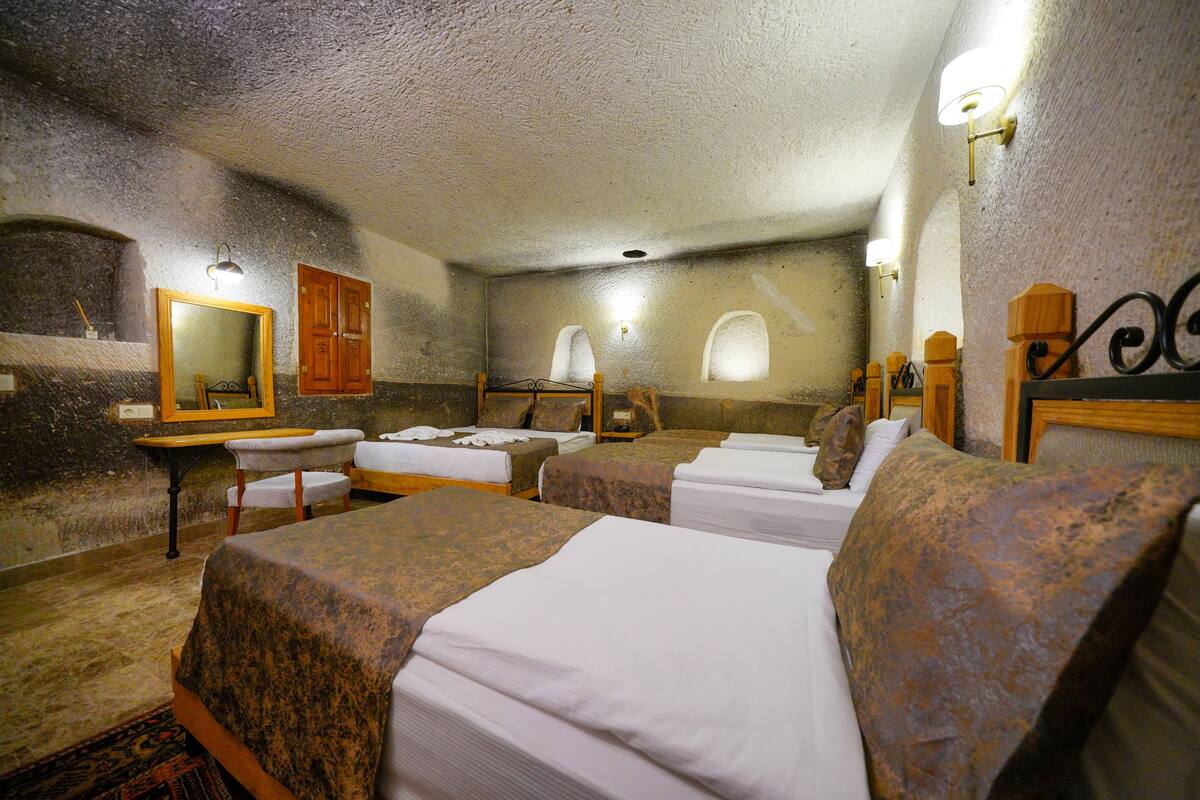 Ein Zimmer mit vier Betten, einem Holztisch, einem Spiegel und Steinwänden.