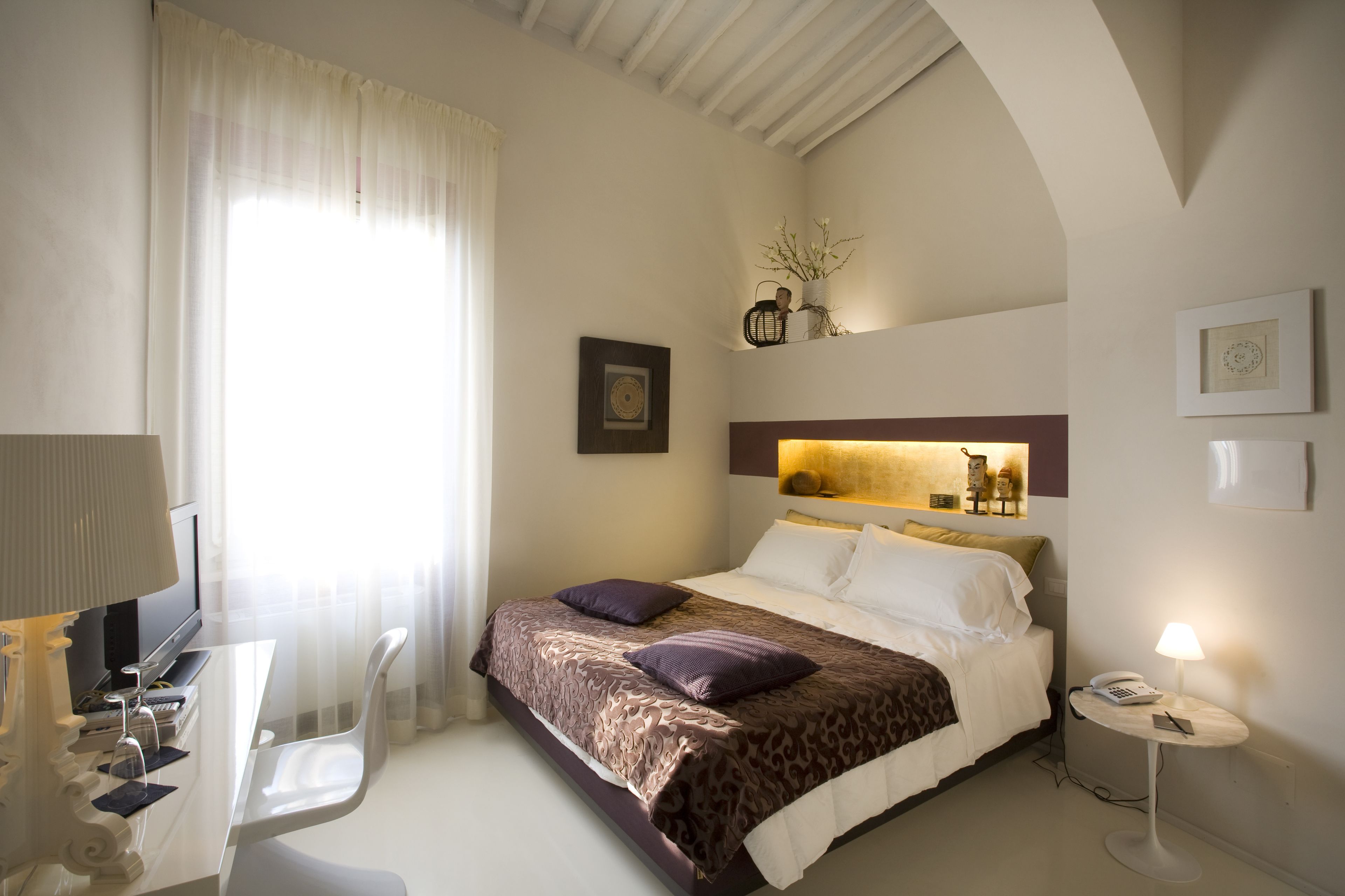 Ein Hotelzimmer mit Bett, Nachttisch, Lampe und Schreibtisch mit Stuhl.