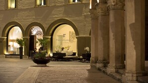 Un bâtiment historique doté d’arches et de colonnes, un espace d’accueil avec un canapé et des plantes en pot, et une enseigne indiquant « PalazzoBontàresi Hotel & Spa ».