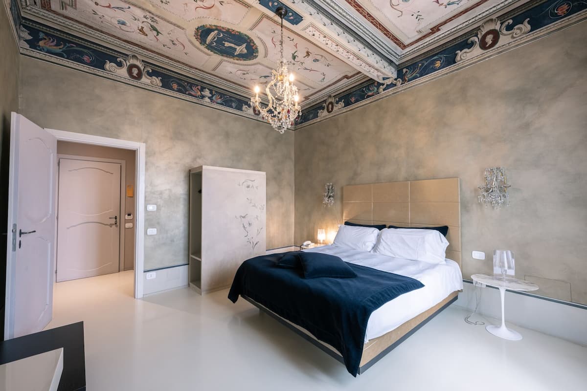 Une chambre d’hôtel moderne avec un grand lit, un lustre, une petite table et une armoire.