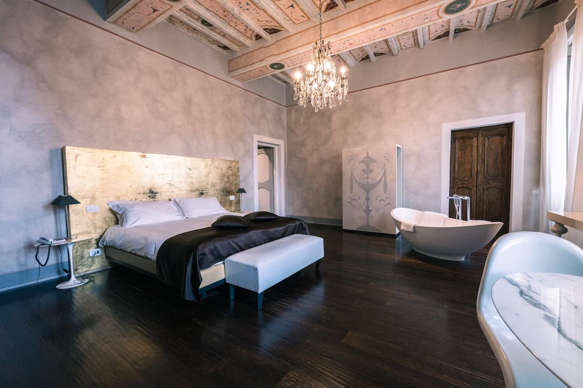 Une chambre spacieuse avec un grand lit, une baignoire moderne et un lustre.