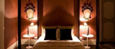 A four-poster bed with a brown headboard and black pillows, flanked by two wall-mounted lamps.