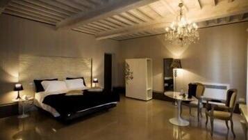 Ein modernes Schlafzimmer mit einem großen Bett, Nachttischen, einer Chandelüster und einer Sitzecke mit Tisch und Stühlen.