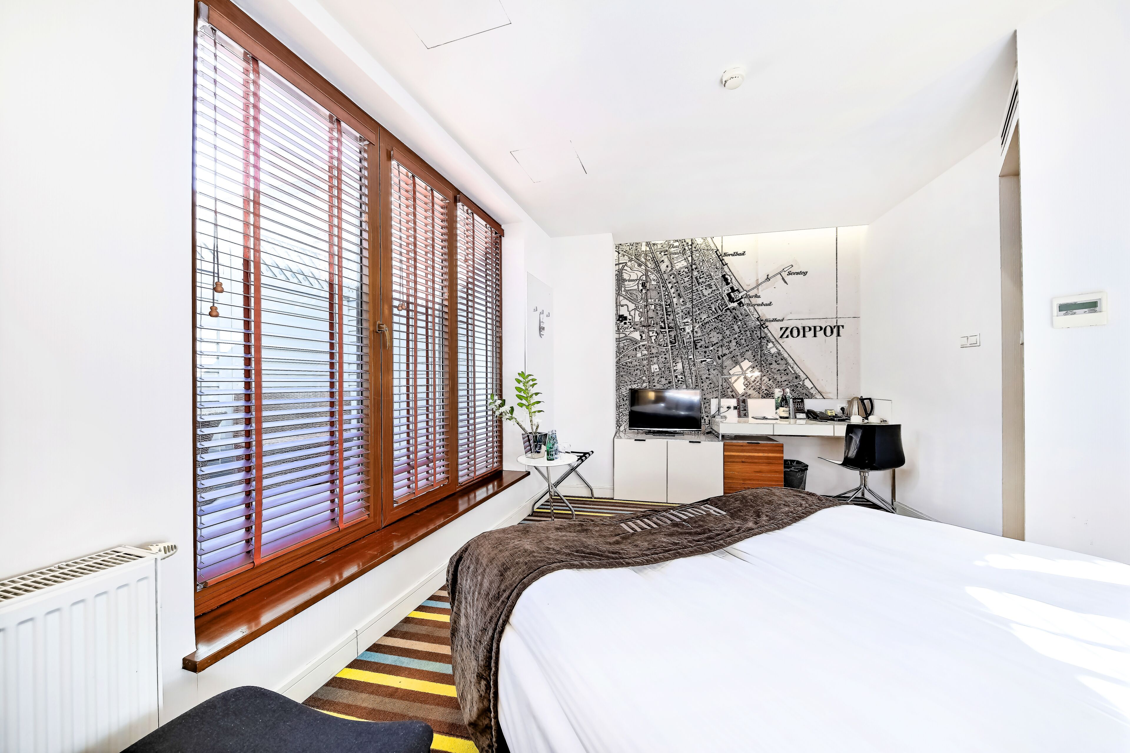 Ein modernes Hotelzimmer mit einem großen Bett, einem Schreibtisch mit Fernseher und einer Stadtlandschaft als Wandbild.