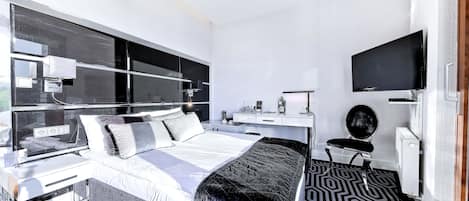 Una habitación de hotel moderna con una cama grande, un escritorio, un televisor de pantalla plana y un ventanal amplio.