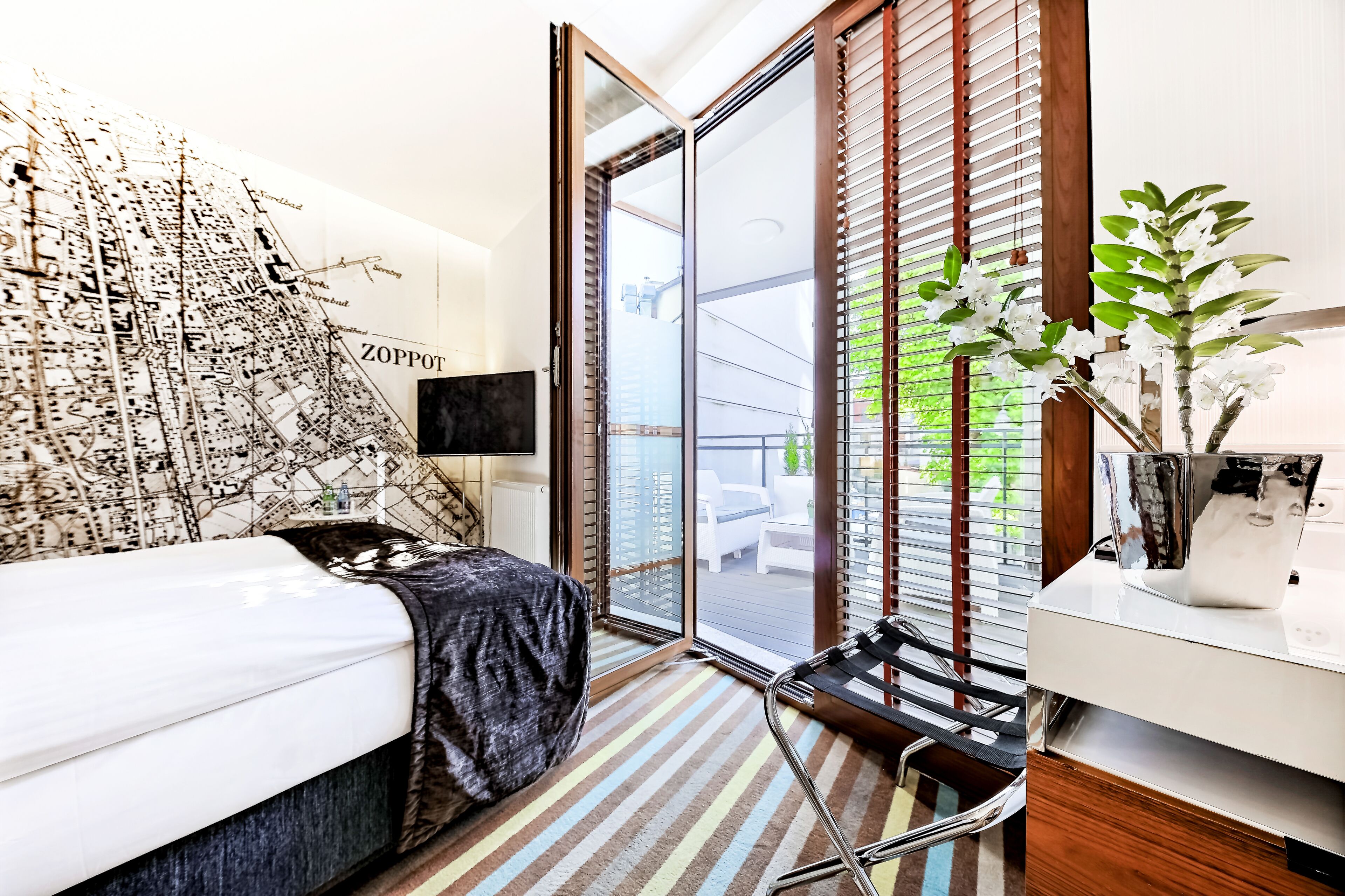 A modern bedroom with a bed, a map wall, a sliding glass door to a balcony, and a small plant on the nightstand.