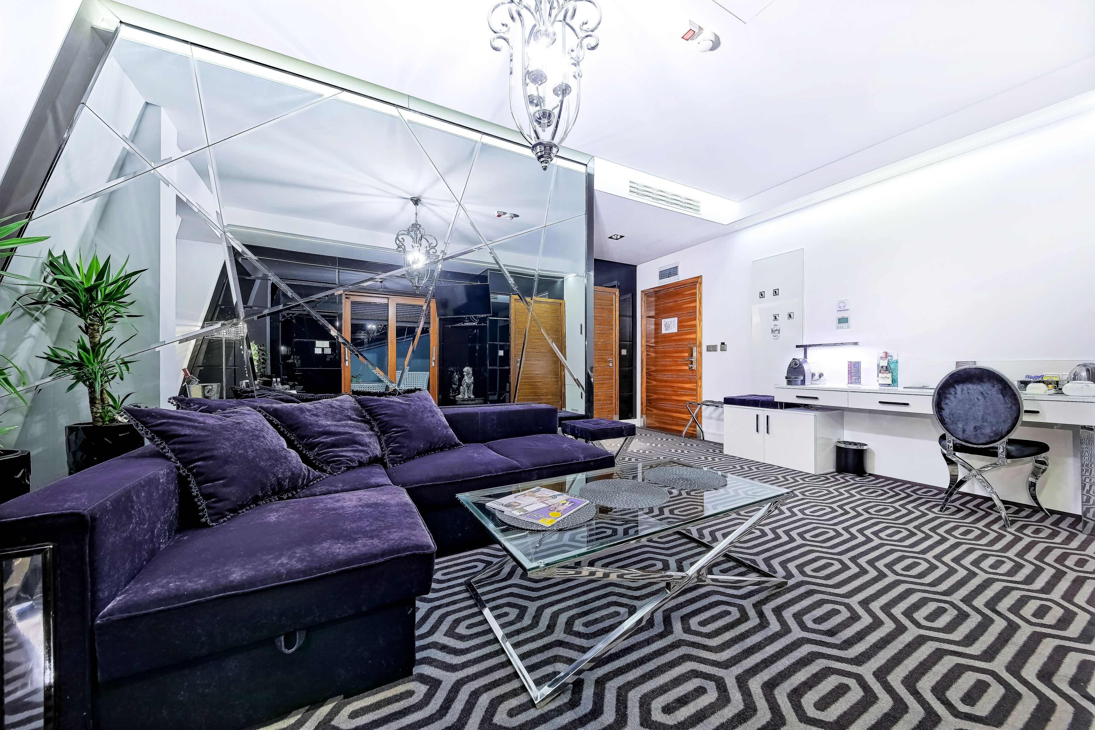 A modern living room with a glass coffee table, purple sofa, and geometric patterned carpet.