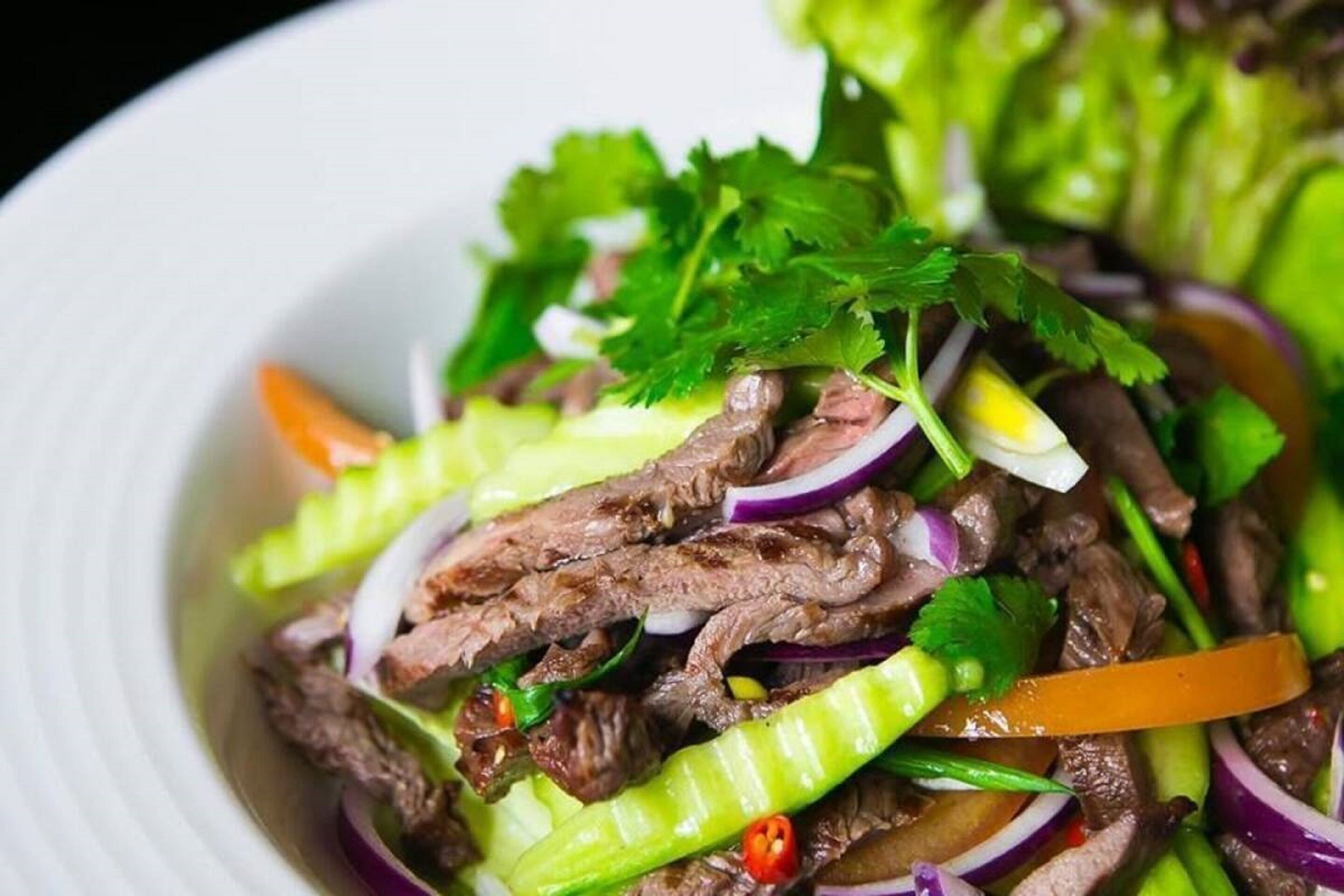 A bowl of beef salad with lettuce, red onions, and cilantro.