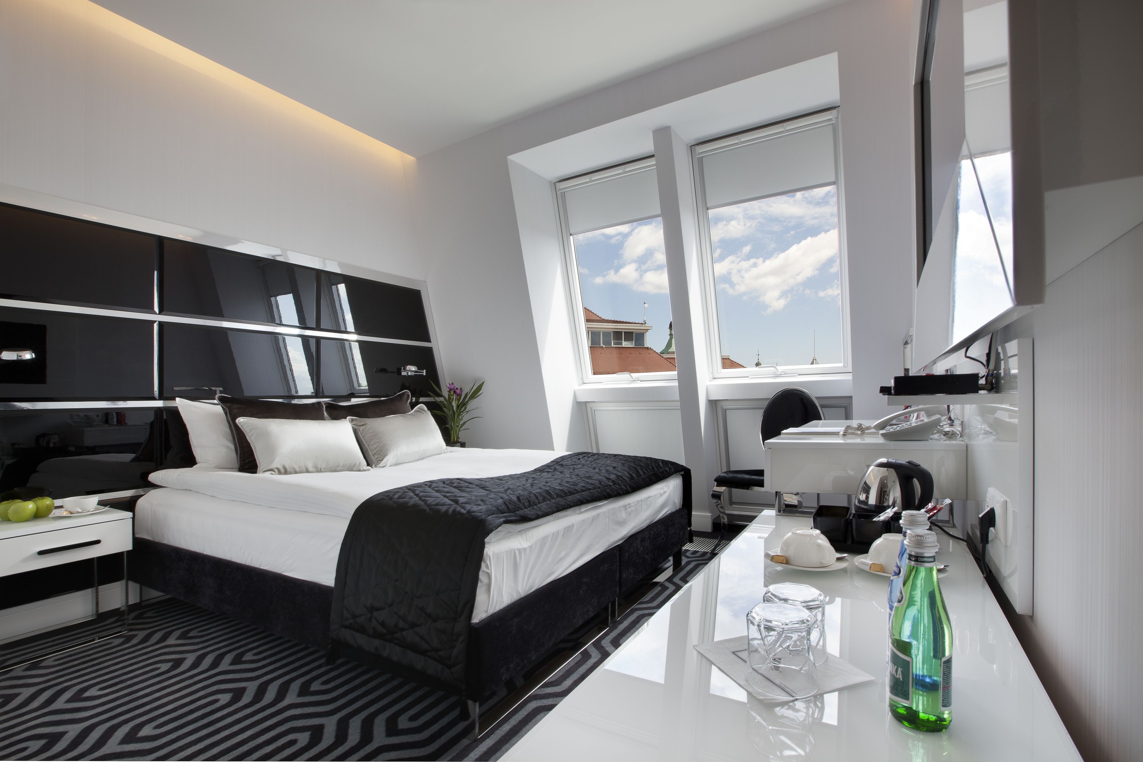A modern hotel room with a large bed, a desk, a chair, and a window with a view of buildings.