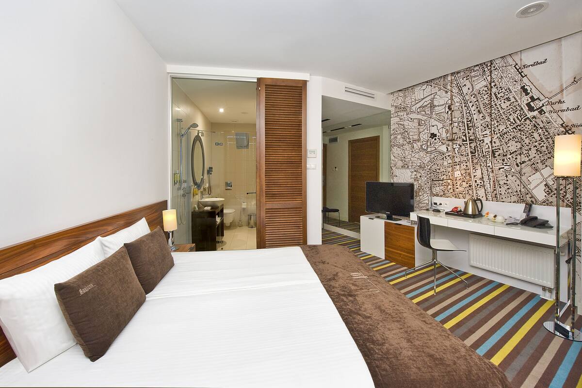 A hotel room with a bed, a desk, a TV, and a map on the wall.