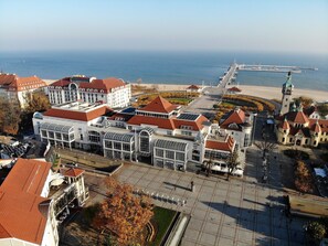 An aerial view of a coastal city with a prominent waterfront promenade, a large white building with a glass facade, and a tower with a clock. - Bayjonn Boutique Hotel (Sopot)