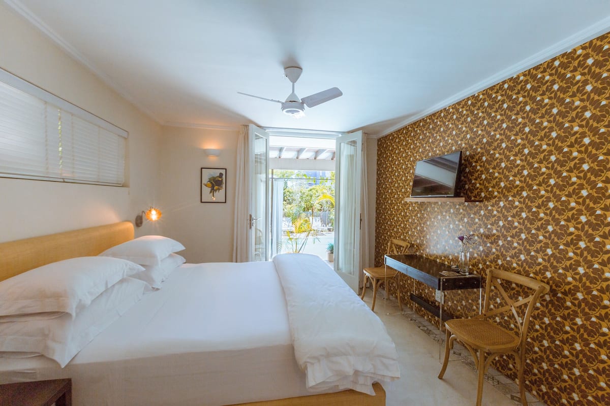 A bedroom with a bed, a desk, a chair, a ceiling fan, and a TV on the wall.