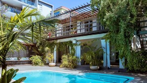 Una piscina rodeada de exuberante vegetación y un espacio al aire libre techado con una pérgola.