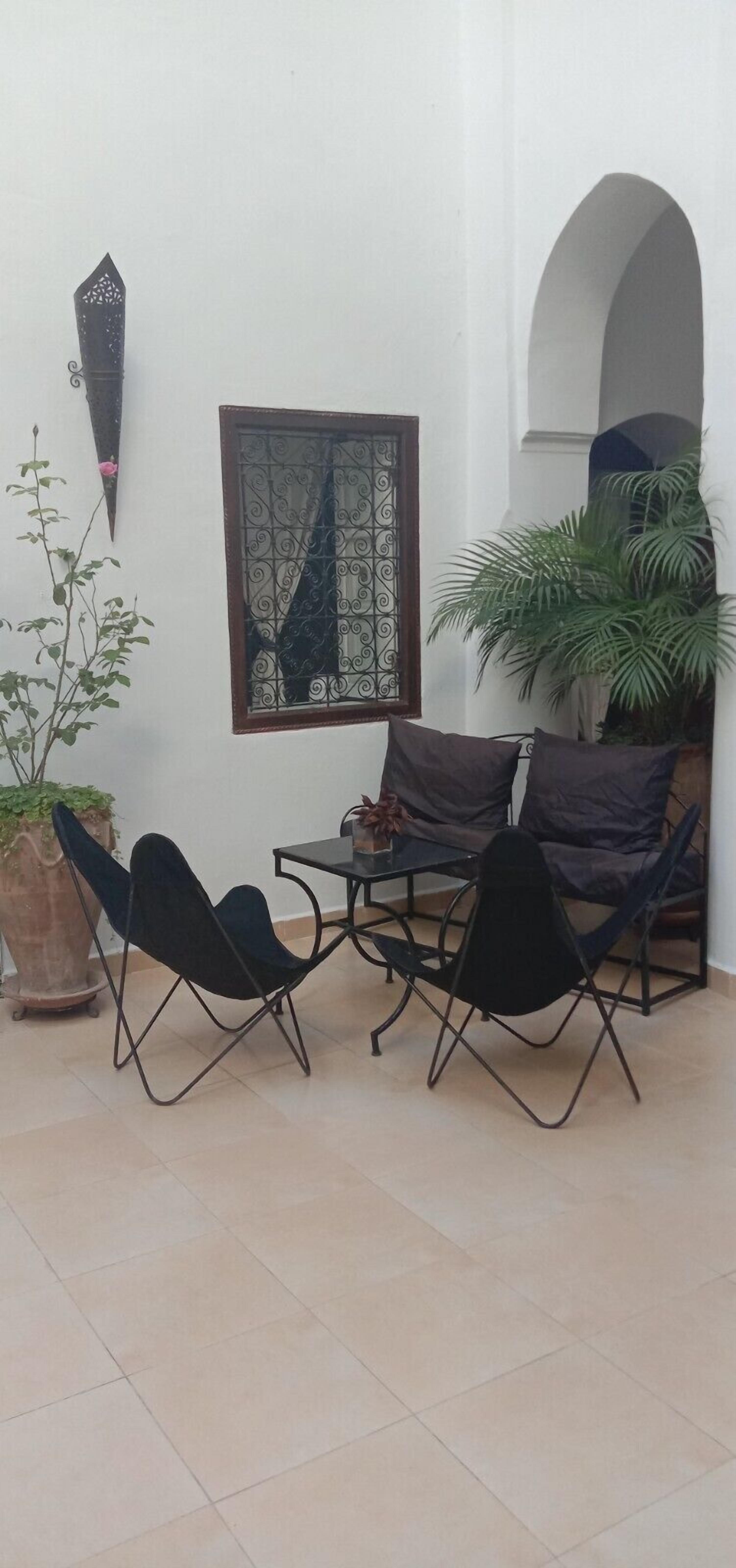 Eine kleine Terrasse mit Tisch und vier Stühlen, einem Blumentopf und einem dekorativen Wandelement.