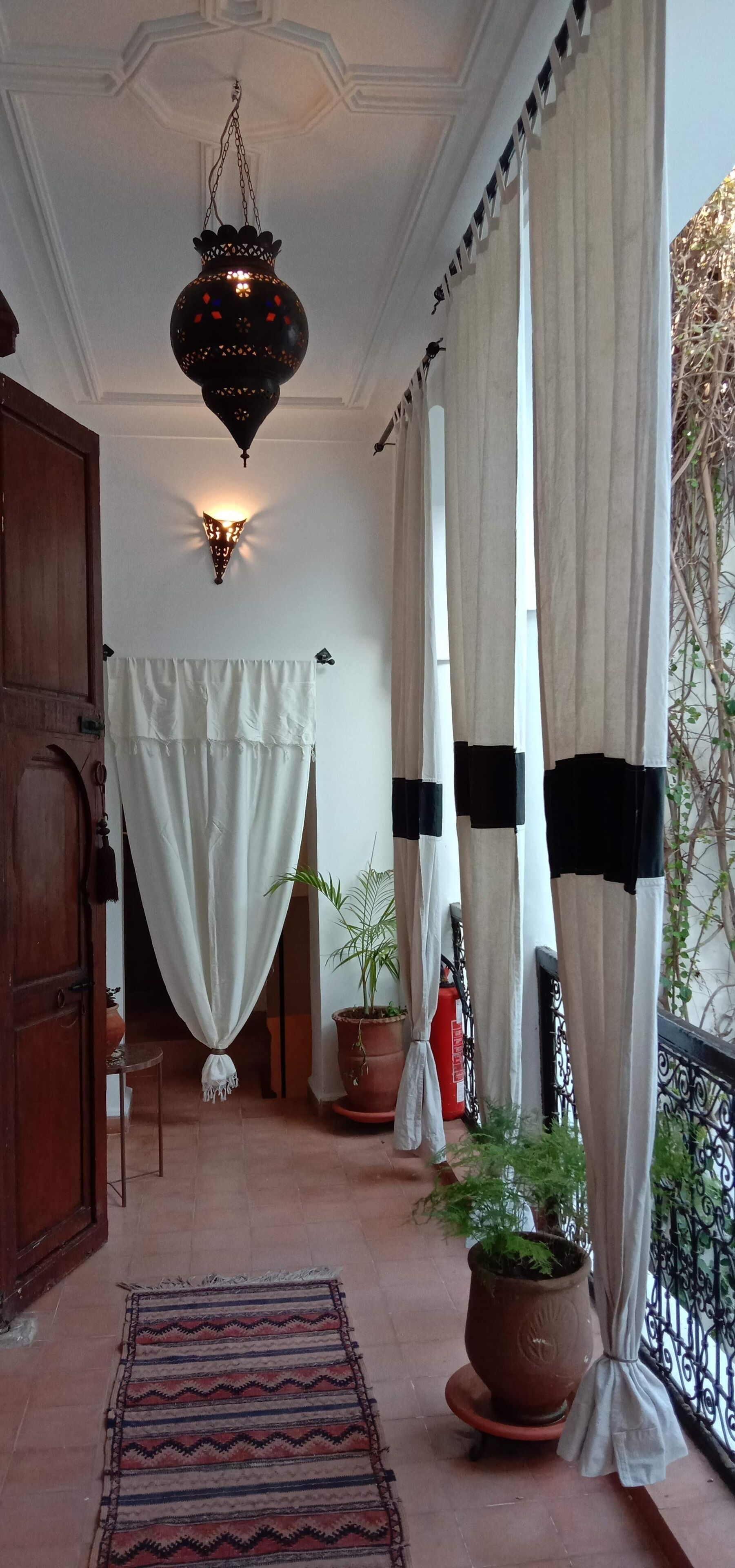 Un pasillo con un farol colgante, cortinas, una planta en maceta y un extintor.