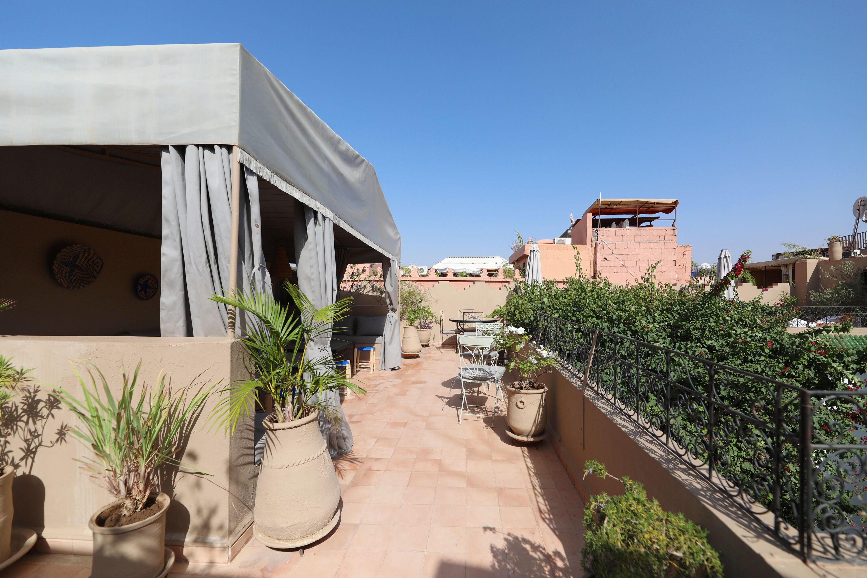 A rooftop terrace with potted plants, outdoor furniture, and a view of adjacent buildings.