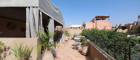 A rooftop terrace with potted plants, outdoor furniture, and a view of adjacent buildings.